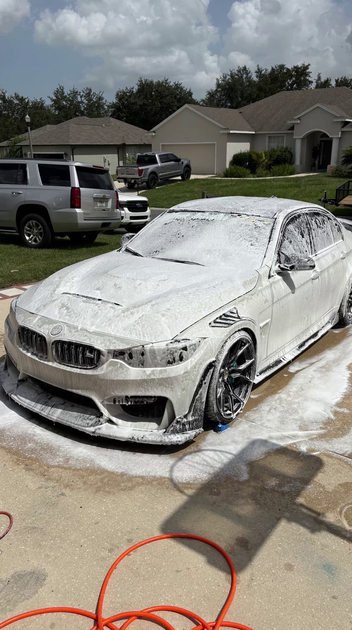 White sedan covered in foam during exterior detail